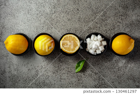 Fresh, juicy lemons and sugar cubes in small black bowls on a gray stone table. Fresh, juicy lemons and sugar cubes in small black bowls on a gray stone table. 130461297