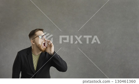 Active man who shouts, announcing advertising information standing on a gray background. Active man who shouts, announcing advertising information standing on a gray background. 130461360
