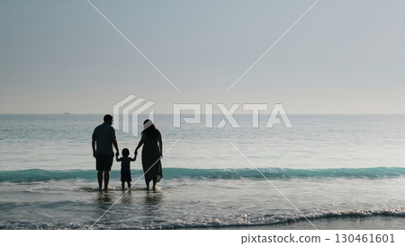 Family silhouette stands together by gentle sea waves under soft sky Family silhouette stands together by gentle sea waves under soft sky 130461601