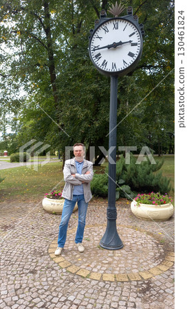 a man stands beside the clock in the square 130461824