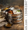 An arranged tiffin meal is set on a dark wooden table. The multiple compartments contain a variety of curries and rice, ready to be served AI generated 130461847