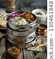 A staged Indian meal features a stacked tiffin container with various dishes. The rustic wooden table is filled with assorted food bowls and naan bread, creating a rich scene AI generated 130461848