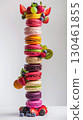 A vertical stack of colorful macarons is topped and surrounded by fresh berries and grapes. The clean, minimalist studio background highlights the vibrant dessert AI generated 130461855