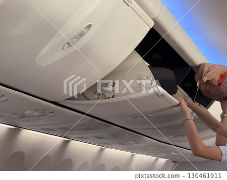 Overhead storage bins inside airplane cabin with luggage and personal items secured for travel. Aviation, mobility, and tourism lifestyle highlighting preparation, safety, and passenger journey. 130461911
