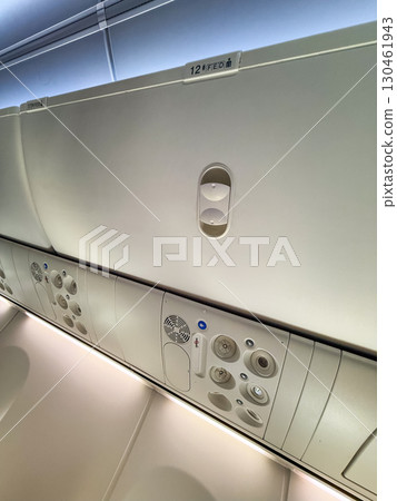 An airplane cabin ceiling with air vents, signs, and compartments above the passenger seats. Travel, aviation, and the technical design of aircraft interiors for comfort and safety. 130461943