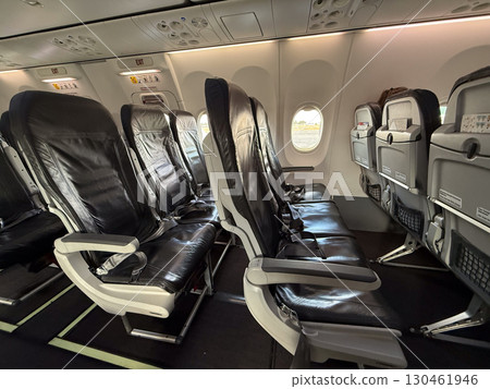 Empty black leather airplane seats next to a window with seatbelts placed on the cushions. Travel, aviation, and the arrangement of seating for passengers on modern flights. 130461946