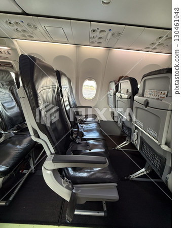Airplane interior with black leather seats arranged near exit row and window section. Travel, mobility, and modern aviation comfort highlighting passenger transport and tourism lifestyle. 130461948