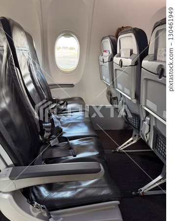 Empty black leather airplane seats next to a window with seatbelts placed on the cushions. Travel, aviation, and the arrangement of seating for passengers on modern flights. 130461949