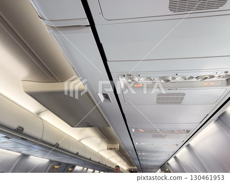 An airplane cabin ceiling with air vents, signs, and compartments above the passenger seats. Travel, aviation, and the technical design of aircraft interiors for comfort and safety. 130461953