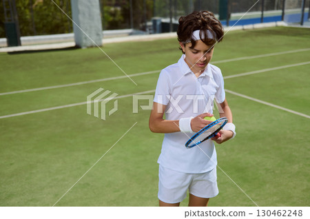 Young Tennis Player Preparing Ball and Racket on Sunny Outdoor Court 130462248
