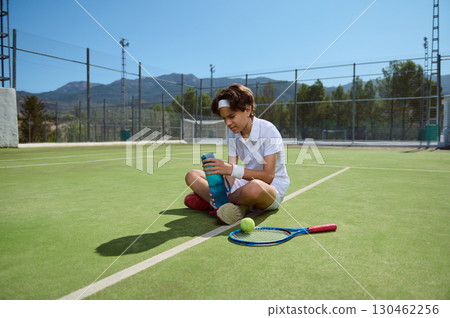 Young Tennis Player Hydrating on Sunny Outdoor Court During a Break Young Tennis Player Hydrating on Sunny Outdoor Court During a Break 130462256