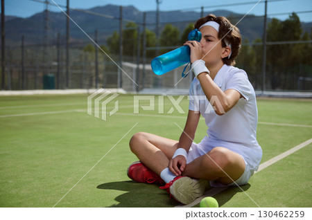 Young Tennis Player Resting and Rehydrating During Outdoor Training Session Young Tennis Player Resting and Rehydrating During Outdoor Training Session 130462259
