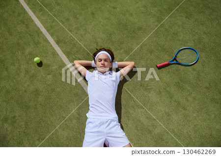 Young Tennis Player Relaxing on Lawn Court With Tennis Gear Nearby 130462269