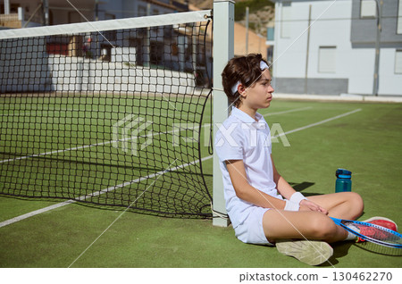 Young Tennis Player Resting Near The Net on a Sunny Day 130462270
