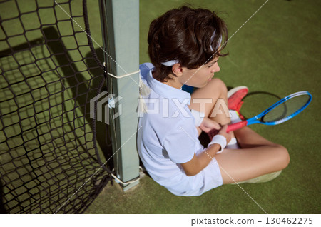 Young Tennis Player Sitting on Court Near Net After a Match Young Tennis Player Sitting on Court Near Net After a Match 130462275