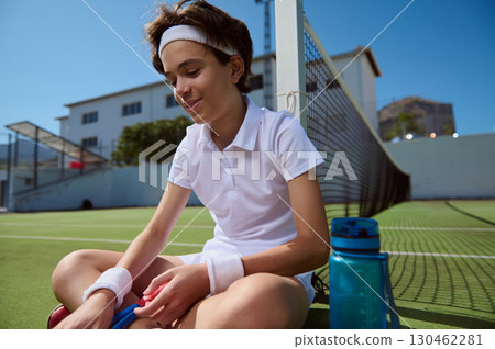Teenage Boy Sitting on Tennis Court With Bottle During a Break Teenage Boy Sitting on Tennis Court With Bottle During a Break 130462281