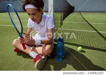 Young Tennis Player Relaxing on Court with Racket and Water Bottle 130462283