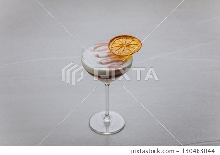 Elegant layered cocktail with citrus garnish and foam in a coupe glass on grey background Elegant layered cocktail with citrus garnish and foam in a coupe glass on grey background 130463044