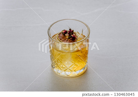 Elegant whiskey cocktail with dried lime and rosebuds in faceted glass on light background Elegant whiskey cocktail with dried lime and rosebuds in faceted glass on light background 130463045