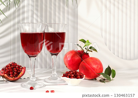 Glasses of red pomegranate wine and grains with ripe pomegranates on a trendy table with palm shades, concept festive party, advertising for a bar and cafe. Source of vitamins for a healthy lifestyle, Glasses of red pomegranate wine and grains with ripe pomegranates on a trendy table with palm shades, concept festive party, advertising for a bar and cafe. Source of vitamins for a healthy lifestyle, 130463157