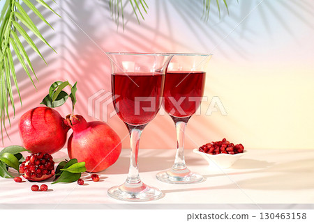 Modern still life with red pomegranate wine and grains with ripe pomegranates on a fashionable table in the shade of palm trees, conceptual holiday party, bar and cafe advertising. Modern still life with red pomegranate wine and grains with ripe pomegranates on a fashionable table in the shade of palm trees, conceptual holiday party, bar and cafe advertising. 130463158