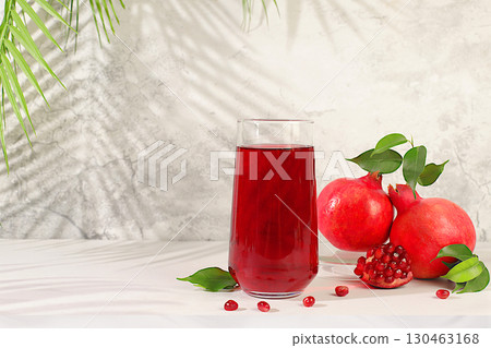 Modern still life with pomegranate juice and grains with ripe pomegranates on a fashionable table in the shade of palm trees, conceptual holiday party, bar and cafe advertising. 130463168