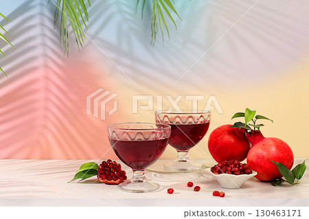 Red pomegranate wine and grains with ripe pomegranates on a trendy table with palm shades, concept festive party, advertising for a bar and cafe. Source of vitamins for a healthy lifestyle, 130463171