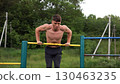 Hardy shirtless sportsman doing push ups on horizontal bar at nature. Strong and muscular guy training at sports ground. Young athletic guy exercising outdoor. Concept of active and healthy lifestyle 130463235
