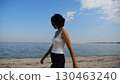 Happy adult woman going on sandy beach near shoreline at sunny day. Beautiful lady walking on seashore with calm waves at background. Concept of summer vacation or holiday. Slow motion 130463240