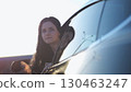 Young beautiful girl leaning out of driver window at modern electric car and looking into camera. Portrait of attractive smiling woman in alternative electrical vehicle. Slow motion 130463247