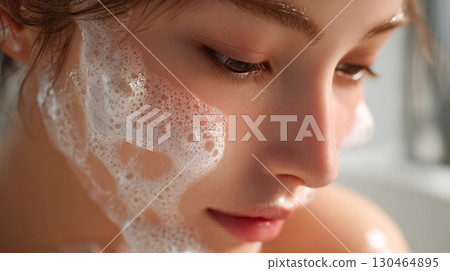 Close-up shot of a woman's face washing her face with foam in the bathroom. Natural light, cleanliness, relaxed atmosphere. 130464895