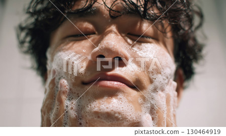 Close-up photo of a man washing his face. Foamy face and relaxed expression in the bathroom. Morning skincare routine. 130464919