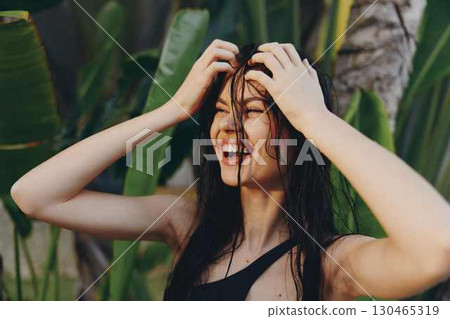 Happy young woman in stylish black swimsuit smiling and holding her hair up in the air on the beach Happy young woman in stylish black swimsuit smiling and holding her hair up in the air on the beach 130465319