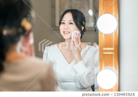 Bride applying makeup in the bridal room of a wedding venue 130465928