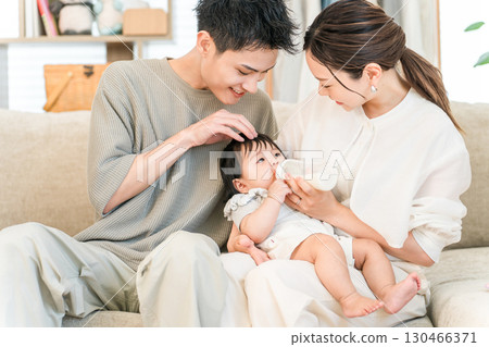 Mom and dad feeding their baby with a bottle on the sofa at home (parental leave) Mom and dad feeding their baby with a bottle on the sofa at home (parental leave) 130466371