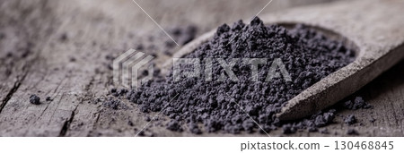 High-quality activated charcoal powder displayed on wooden spoon against rustic backdrop High-quality activated charcoal powder displayed on wooden spoon against rustic backdrop 130468845