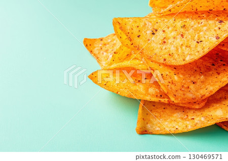 Crunchy tortilla chips stacked on a turquoise background with spicy seasoning for snack time enjoyment Crunchy tortilla chips stacked on a turquoise background with spicy seasoning for snack time enjoyment 130469571