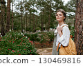 Young woman in casual outfit with a backpack, smiling outdoors surrounded by greenery and flowers, capturing a serene moment in nature 130469816