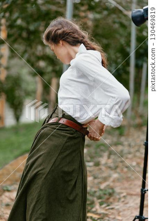 Elegant outdoor portrait of a female model wearing a white blouse and green skirt, showcasing natural beauty and emotional expressiveness in a serene garden background 130469819