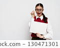 Happy girl in glasses holding a blank sign, smiling and pointing at it with a pencil, wearing a red sweater, on a plain white background Engaging and cheerful expression 130471301