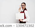 surprised girl with open notebook and pen, wearing glasses, standing against a light gray background, dressed in a red vest and white shirt, showing excitement in her expression 130471302