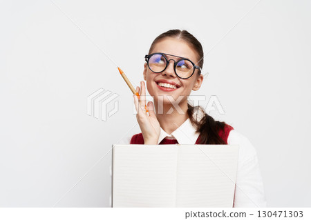 Smiling student with glasses holding a notebook and a pencil, looking thoughtful against a white background Engaging expression indicating creativity and inspiration Smiling student with glasses holding a notebook and a pencil, looking thoughtful against a white background Engaging expression indicating creativity and inspiration 130471303