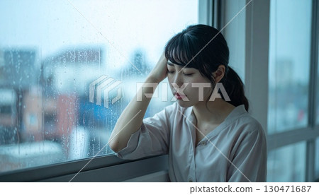 A woman holding her head by the window on a rainy day 130471687