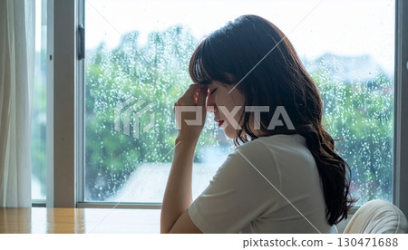 A woman in thought with the rain outside the window behind her 130471688