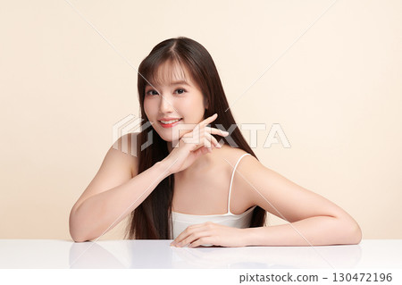 A beautiful young Asian woman with clean, fresh skin against a beige background. Skincare, facial treatment, cosmetology, beauty, and spa. An elegant portrait of an Asian woman. 130472196