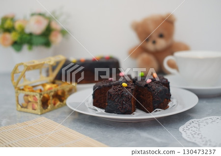 Chocolate cake slices on a white plate with decorations, next to a chest with gold and a cup of coffee 130473237