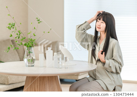 一位年輕的亞洲女性在家裡的客廳一邊照鏡子一邊做頭髮護理 130473444