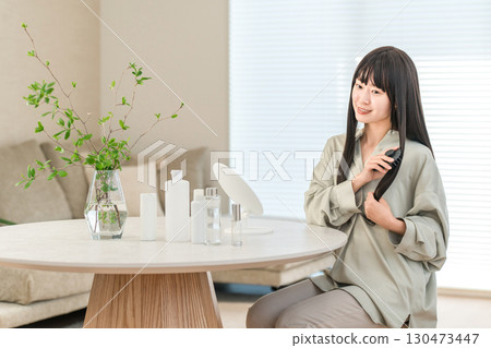 A young Asian woman doing hair care while looking in the mirror in the living room at home 130473447