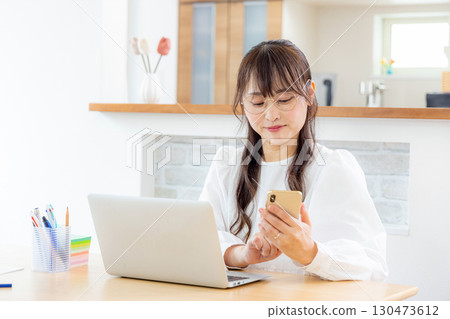 Teleworking woman looking at her smartphone Teleworking woman looking at her smartphone 130473612