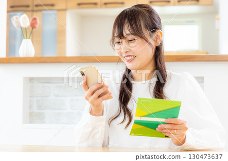 A woman using a smartphone and a household account book 130473637